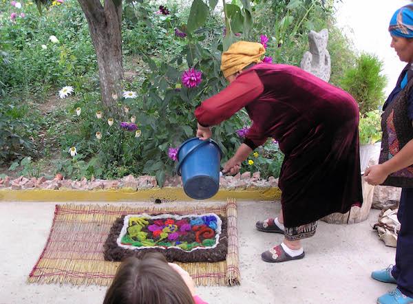 Feltmaker pouring hot water over a design made with dyed wool on a natural beaten wool base.