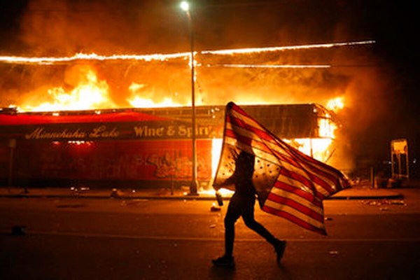 Minneapolis protester carries the carries a US flag upside down, a sign of distress, Thursday, May 28, 2020. (AP Photo/Julio Cortez.)